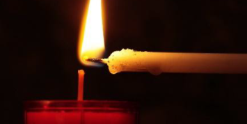 Ein Teelicht wird mit einer Stabkerze angezündet.